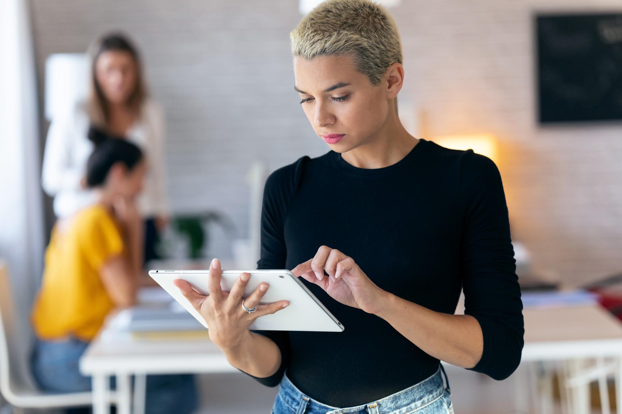 Jeune femme concentrée utilisant sa tablette numérique dans son bureau.